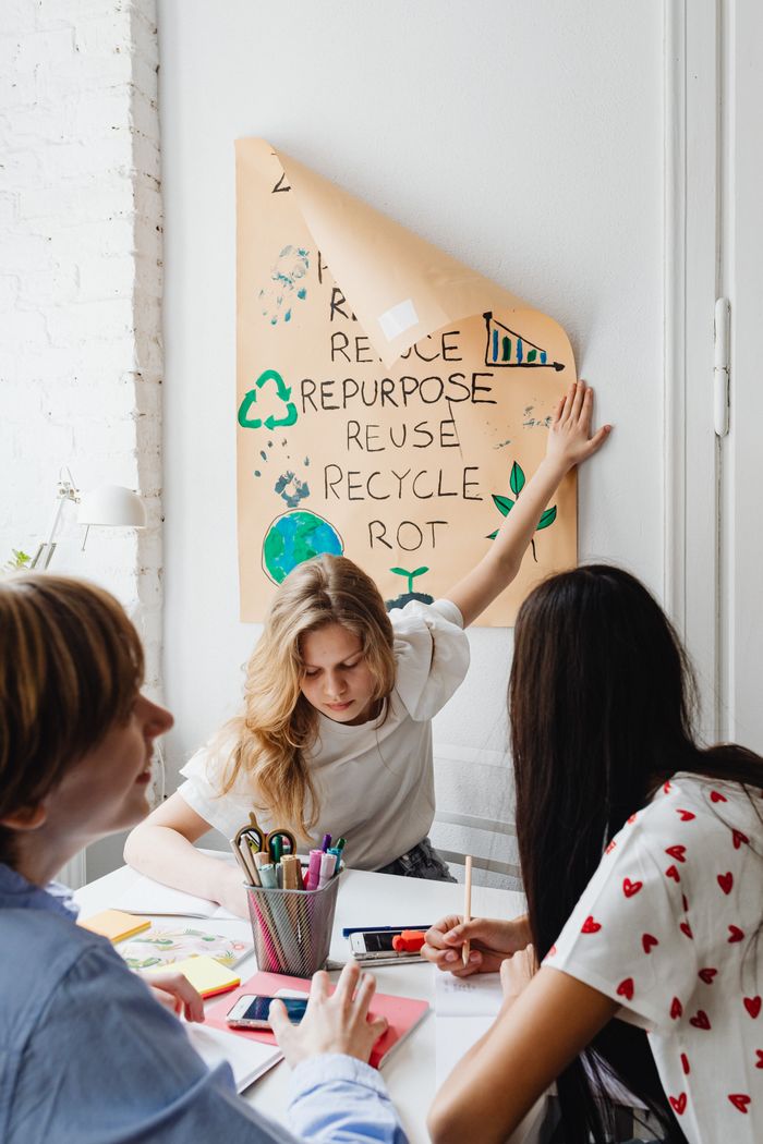 Three teenagers discuss an eco-friendly school project with a focus on recycling and sustainability indoors.
